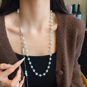 Elegant long French style pearl necklace sweater chain worn over a stylish brown cardigan