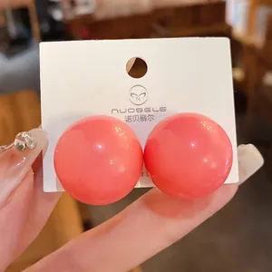 Primo piano di vistosi orecchini a perno sferici color corallo su cartoncino bianco