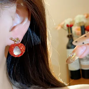 Close-up detail of a creative red lychee-shaped zircon earring worn on a female ear.