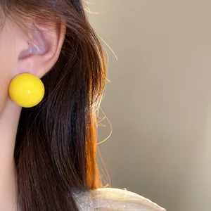 Primo piano di un orecchino a bottone a sfera giallo brillante sull'orecchio di modella.