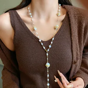French style long sweater chain necklace featuring irregular pearls worn on brown knitwear.