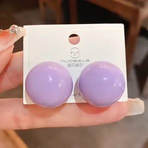 Dettaglio macro di orecchini a bottone a sfera viola lucidi su scheda bianca.