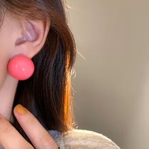 Vista macro dettagliata di orecchini a perno con grandi sfere rosa lucide indossati sul modello