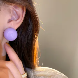 Primo piano di un orecchino a sfera viola lucido indossato da una modella con luce calda