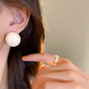 Dettaglio ravvicinato di grandi orecchini a perno a sfera color crema indossati da una modella
