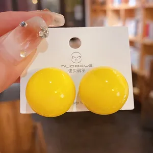 Primo piano di orecchini a perno a sfera gialla lucida su supporto di cartone bianco.