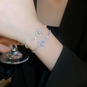 Elegant detail showing two delicate zircon-encrusted four-leaf flower bracelets on a wrist.