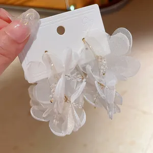 Primer plano de elegantes pendientes de flores de tul blanco con aros dorados y cristales