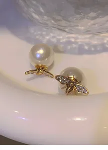 Dettaglio di orecchini vintage a forma di ape con ali di cristallo e grandi perle bianche