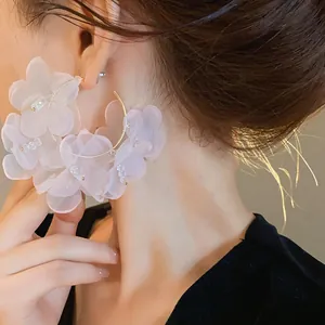 Primer plano de pendientes de aro dorados con flores de organza blancas y cristales.