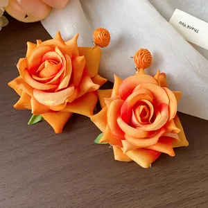 Primer plano de pendientes de rosa de tela naranja con detalles de rafia