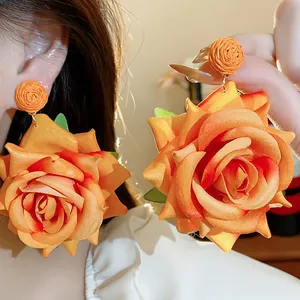 Primer plano de pendientes de rosa de tela naranja con tuercas de rafia tejida