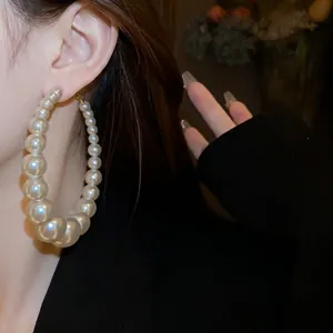 Elegante übergroße weiße Perlen-Creolen mit Größenverlauf an einem Model getragen.