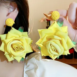 Detalle de pendientes de flores de tela amarilla con bola de rafia tejida.