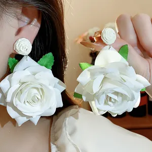 Detalle de elegantes pendientes de rosa de tela blanca con hojas verdes y broches de flor
