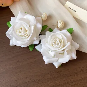 Detalle de pendientes de rosa de tela blanca con elegantes cierres envueltos en rafia