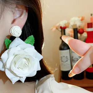 Primer plano de pendientes de rosa de tela blanca con hojas verdes