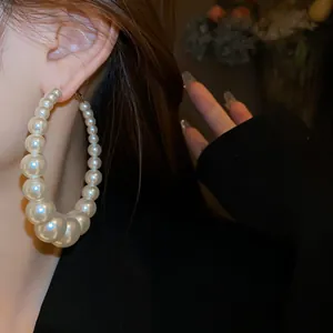 Detailansicht eines übergroßen Perlen-Creolen-Ohrrings, getragen von einem Modell für Mode