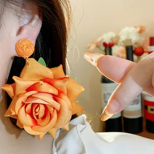 Detalle de un pendiente de rosa de tela naranja con base de rafia trenzada.