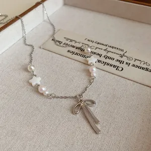 Detail shot of an elegant silver bow pendant necklace with white pearls and star beads.