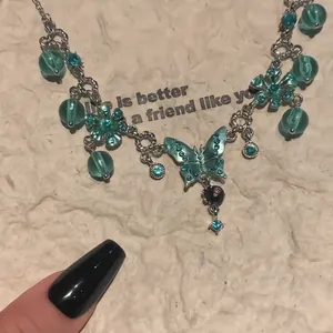 Close-up of turquoise enamel butterfly necklace with blue crystals and green beads.
