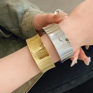 Close-up detail of stylish wide metal cuff bracelets in gold and silver worn on a wrist