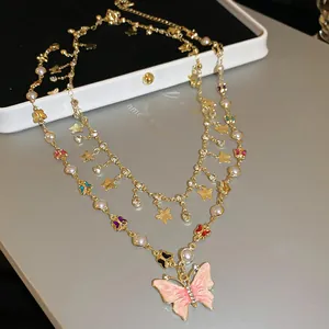 Close-up of layered butterfly necklace with pink enamel pendant and elegant pearls.
