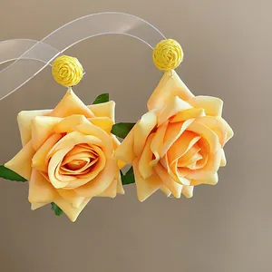 Detalle de elegantes pendientes de rosa de tela amarilla con detalles de rafia para mujer