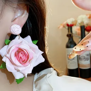 Primer plano detallado de un pendiente de rosa de tela rosa con hojas verdes en modelo