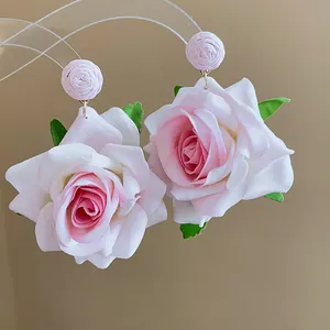 Detalle de pendientes de rosas de tela rosa con hojas verdes y pernos de rafia.
