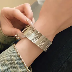 Close-up of a wide silver metallic cuff bracelet with vertical ridges and dot textures.