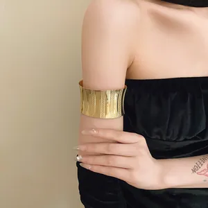 Detailed view of a wide gold metal arm cuff with vertical textured patterns on a model's arm.