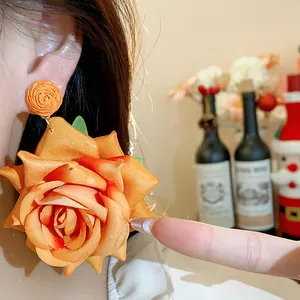 Primer plano detallado de un pendiente de rosa de tela naranja que muestra su gran tamaño y textura.