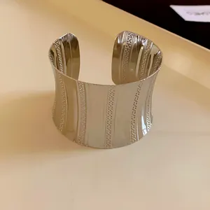 Detailed macro view of a silver-toned metal cuff bracelet with vertical engraved patterns