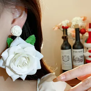 Detalle de pendientes grandes de rosa de tela blanca usados por una modelo para un look dulce