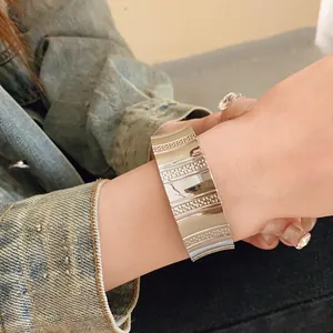 Stylish wide silver metallic open cuff bracelet with textured ribbed design details.