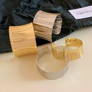 Close-up of gold and silver metal cuff bracelets with textured stripe patterns.