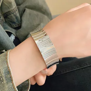 Detail view of a wide silver textured metal cuff bracelet worn on a model's wrist