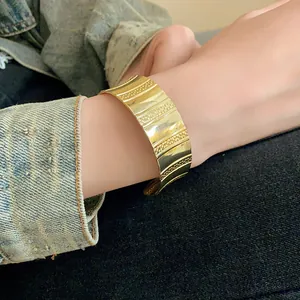 Close-up view of chunky gold wide cuff bracelet featuring textured vertical stripes