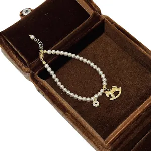 Elegantes Perlenarmband mit Schaukelpferd- und Zirkon-Münzanhängern auf einer braunen Samtbox.