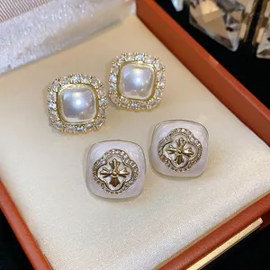 Close-up view of elegant square zircon pearl studs and floral enamel earrings in a gift box