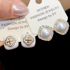 Macro detail view of French-style zircon flower and square pearl stud earrings on display cards.