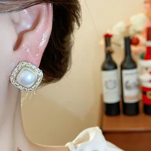 Close-up detail of a square pearl stud earring with zircon halo worn on a model's ear.