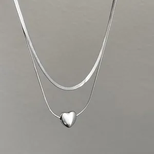 Detailed macro view of a silver double-layered necklace with heart pendant and snake chain
