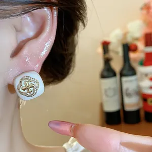 Detailed macro view of square white stud earring featuring a gold flower cross and zircon border