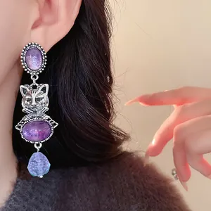 Detail view of vintage-style silver cat earrings with textured purple resin stones.