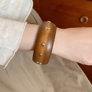 Close-up of vintage brown wooden bangle with silver star and dot studs on wrist.