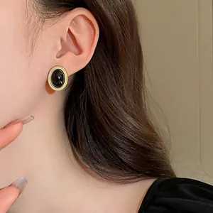 Close-up of elegant vintage oval black and gold earrings worn by a model in detail.