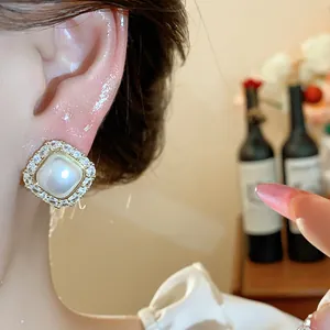 Macro detail view of elegant square pearl stud earring with zircon halo worn on ear
