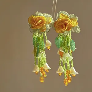 Close-up of Mori-style floral earrings with yellow roses and green beaded tassels
